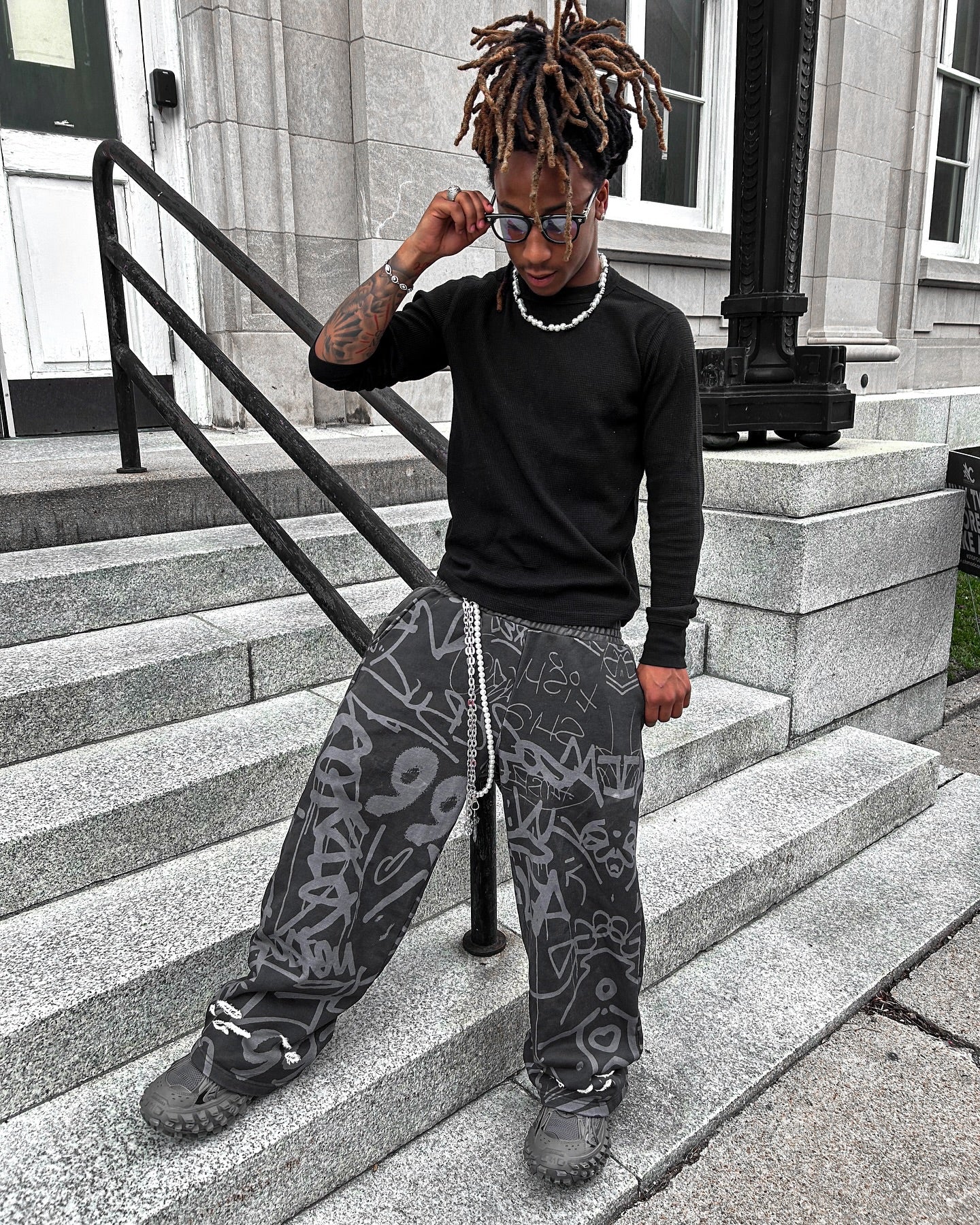 Model wearing black vandalizm sweats with graffiti prints, styled casually on outdoor steps.